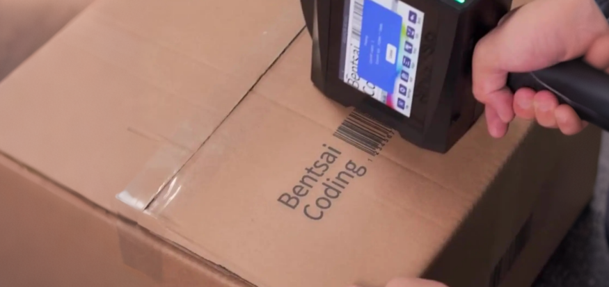 Warehouse-worker-using-a-Bentsai-handheld-inkjet-printer-to-print-a-barcode-directly-onto-a-shipping-box